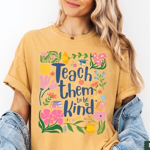 May include: Mustard yellow t-shirt with a floral design and the text "Teach them to be kind".