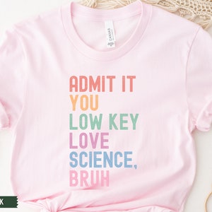 May include: A soft pink t-shirt with the text "ADMIT IT YOU LOW KEY LOVE SCIENCE, BRUH" in rainbow colors.