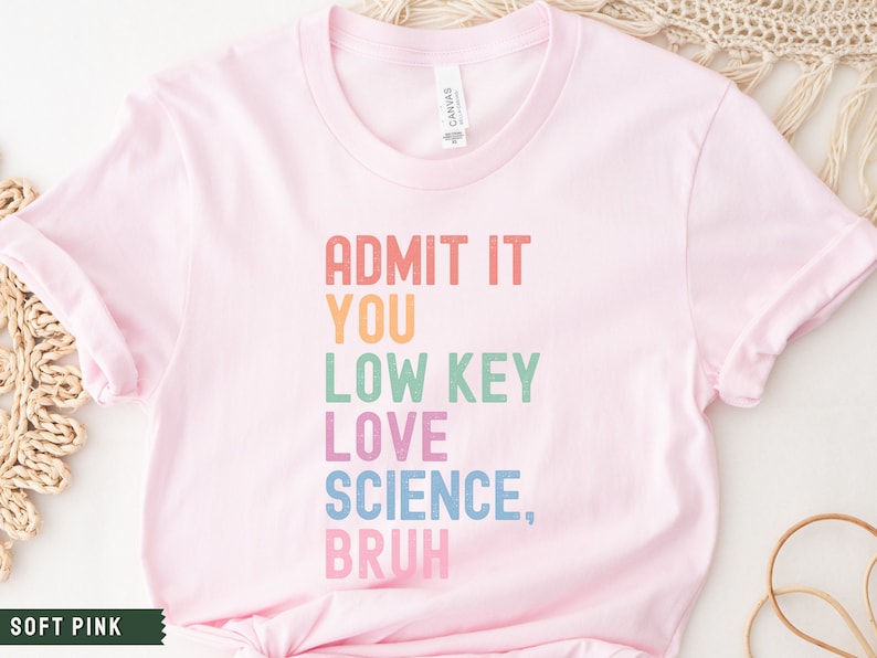 May include: A soft pink t-shirt with the text "ADMIT IT YOU LOW KEY LOVE SCIENCE, BRUH" in rainbow colors.