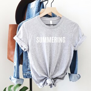 May include: Gray t-shirt with the word "SUMMERING" printed in white on the front.