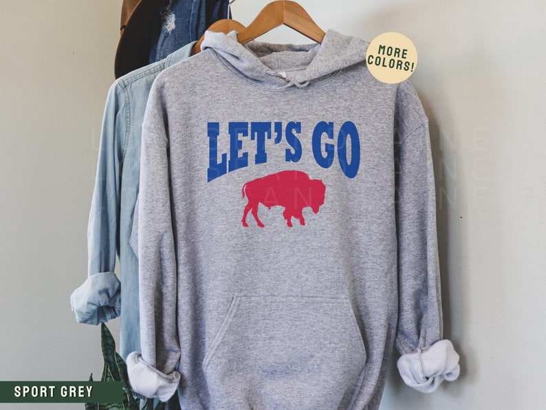 May include: A gray hooded sweatshirt with the text "LET'S GO" in blue and red letters. A red buffalo silhouette is below the text.