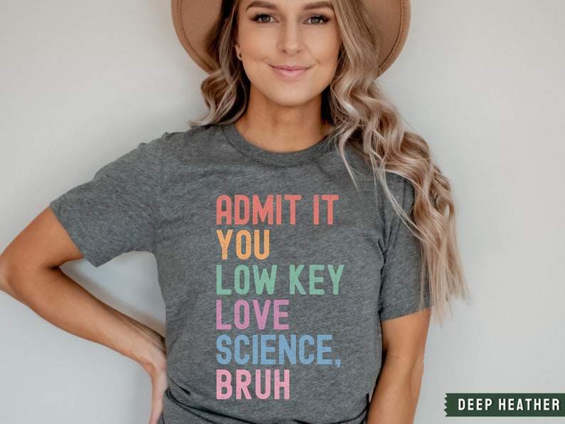 May include: A dark heather grey t-shirt with the text "ADMIT IT YOU LOW KEY LOVE SCIENCE, BRUH" in rainbow colors.