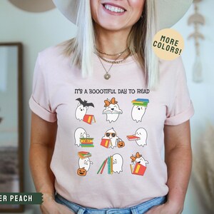 May include: A pink t-shirt with the text "It's a Bootiful Day to Read" and a graphic of ghosts reading books. The ghosts are wearing hats, sunglasses, and bows.