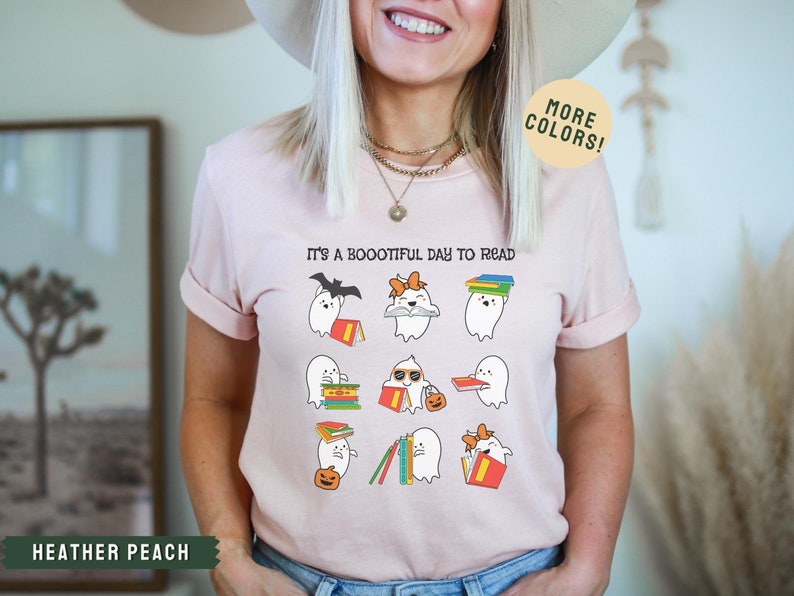 May include: A pink t-shirt with the text "It's a Bootiful Day to Read" and a graphic of ghosts reading books. The ghosts are wearing hats, sunglasses, and bows.