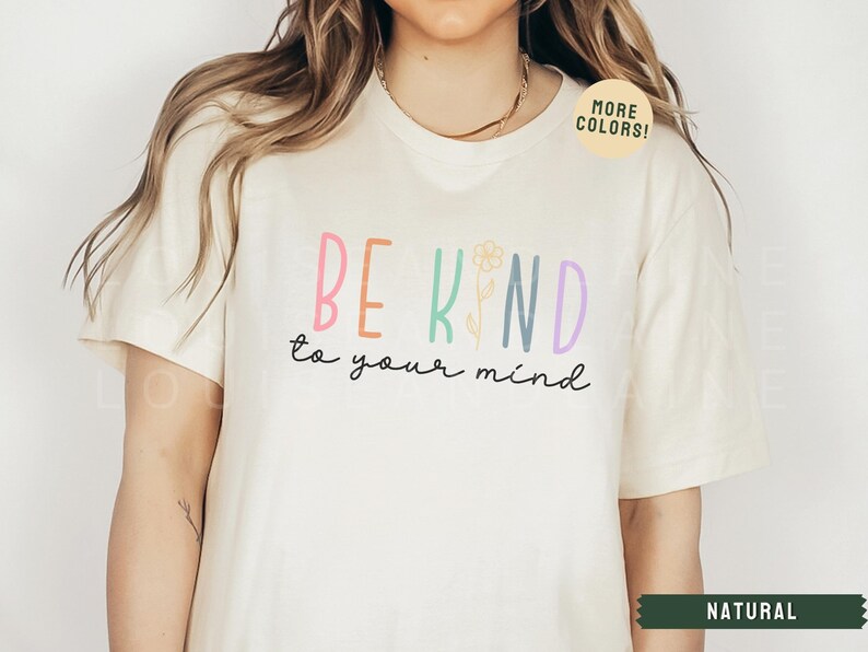 May include: A white t-shirt with the text "BE KIND to your mind" in colorful letters with a flower graphic. The text "MORE COLORS!" is in a green circle on the shirt.