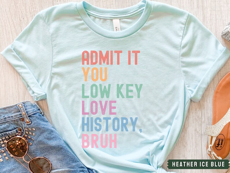 Puede incluir: Una camiseta azul claro con el texto "ADMIT IT YOU LOW KEY LOVE HISTORY, BRUH" en colores arco&iacute;ris.