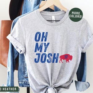 May include: Gray t-shirt with the text "OH MY JOSH" in blue and a red buffalo with the number 17 on it. The text "MORE COLORS!" is in a green circle in the top right corner.
