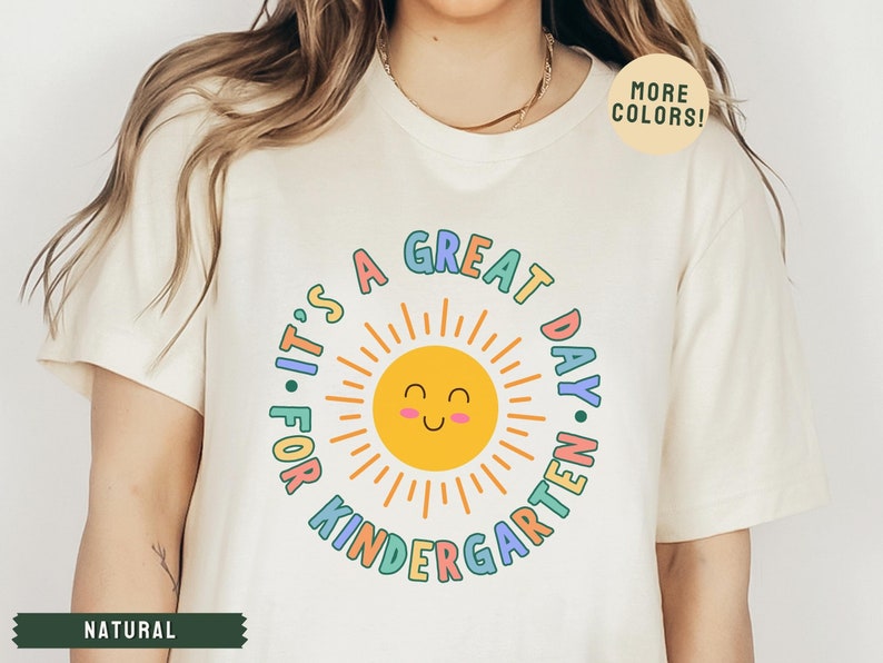 May include: A white t-shirt with a colorful graphic that says "It's a Great Day for Kindergarten" with a smiling sun in the center.
