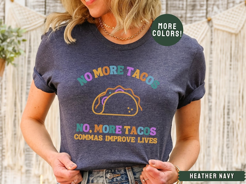May include: Heather navy blue t-shirt with a colourful graphic of a taco and the text "NO MORE TACOS, COMMAS IMPROVE LIVES".