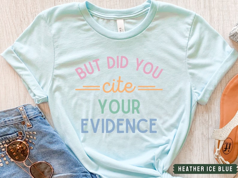 Op de afbeelding: Een lichtblauw T-shirt met de tekst "BUT DID YOU -cite- YOUR EVIDENCE" in kleurrijke letters.