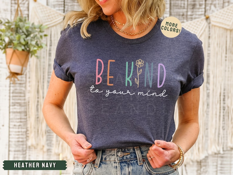 May include: A heather navy blue t-shirt with the text "Be Kind to your mind" in colorful letters with a small flower graphic.