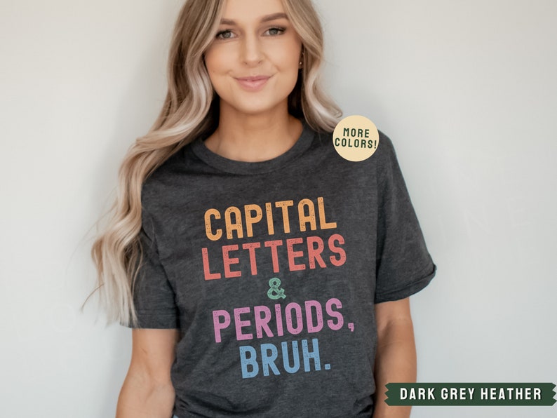 Puede incluir: Camiseta de color gris oscuro jaspeado con el texto "CAPITAL LETTERS & PERIODS, BRUH." en colores arco&iacute;ris. El texto est&aacute; en una fuente de estilo vintage.