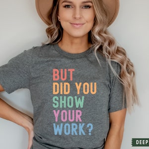 May include: A dark heather grey t-shirt with the text "BUT DID YOU SHOW YOUR WORK?" printed in rainbow colors.