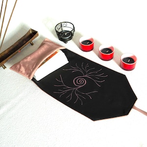 May include: A black fabric tarot card pouch with a pink spiral tree design, featuring a metallic rose-gold satin flap. The set includes a brass incense holder, a black metal candle holder, and three red glass votive candles with black wax.