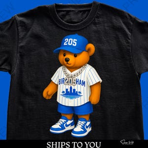 May include: Black t-shirt with a cartoon bear wearing a blue baseball cap with "205", a silver chain, and a baseball jersey with "BIR205HAM" and a city skyline graphic. The bear is also wearing blue shorts and trainers.