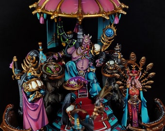 May include: A miniature figurine set depicting a fantasy scene with a seated demon figure wearing a purple and blue robe, a gold crown, and a jeweled necklace. The demon is holding a staff with a blue orb at the top. The scene is set on a platform with a pink canopy and gold accents. There are two other figures standing on the platform, one wearing a pink robe and the other wearing a blue robe.