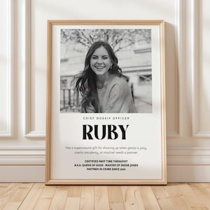 Puede incluir: Un marco con una impresión en blanco y negro. Presenta una foto de una mujer sonriente y el texto "CHIEF GOSSIP OFFICER" sobre el nombre "RUBY". También incluye calificaciones humorísticas.