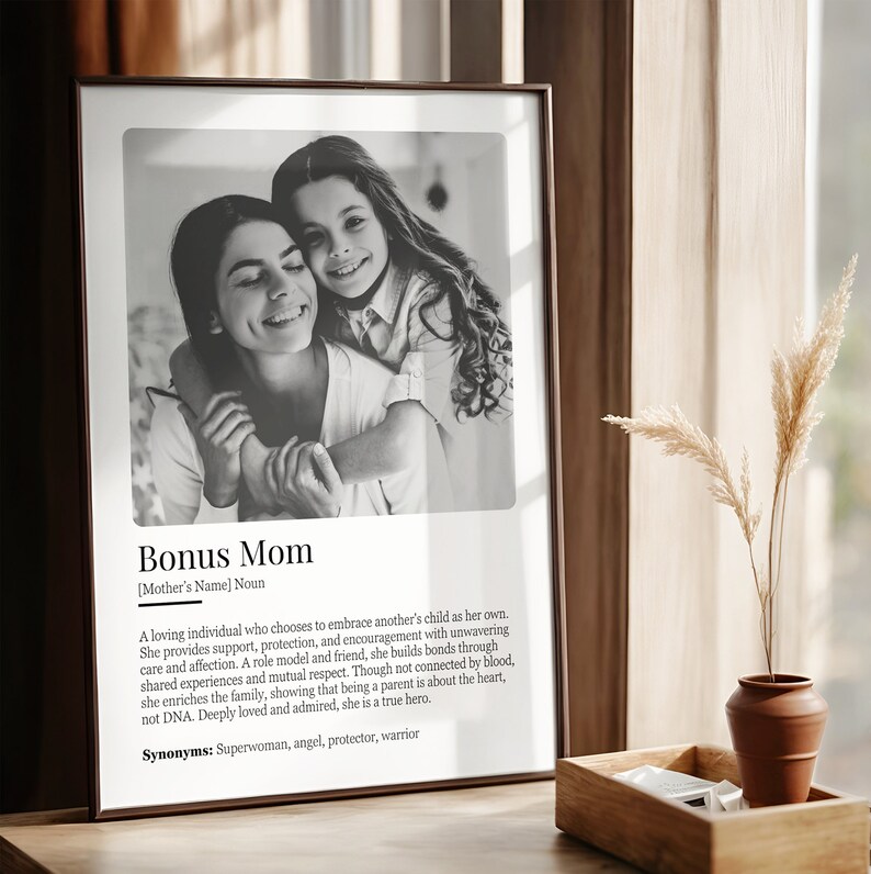 May include: Black and white photo of a woman and a young girl hugging. The photo is in a frame with a white background and text that reads "Bonus Mom [Mother's Name] Noun. A loving individual who chooses to embrace another's child as her own. She provides support, protection, and encouragement with unwavering care and affection. A role model and friend, she builds bonds through shared experiences and mutual respect. Though not connected by blood, she enriches the family, showing that being a parent is about the heart, not DNA. Deeply loved and admired, she is a true hero. Synonyms: Superwoman, angel, protector, warrior"
