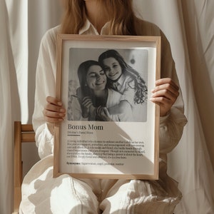 May include: A black and white photo of a woman and a girl hugging. The photo is in a wooden frame with a white background. The text below the photo reads "Bonus Mom [Mother's Name] Noun A loving individual who chooses to embrace another's child as her own. She provides support, protection, and encouragement with unwavering care and affection. A role model and friend, she builds bonds through shared experiences and mutual respect. Though not connected by blood, she enriches the family, showing that being a parent is about the heart, not DNA. Deeply loved and admired, she is a true hero. Synonyms: Superwoman, angel, protector, warrior"