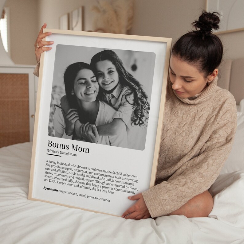 May include: Black and white photo of two women hugging. The photo is framed and has a definition of "Bonus Mom" with synonyms below the photo.