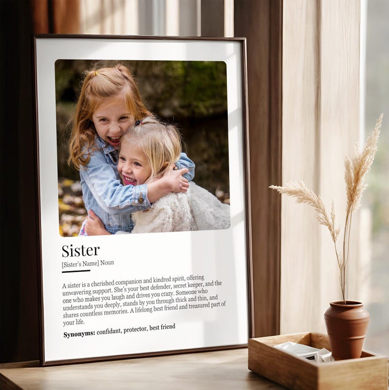 Puede incluir: Una impresi&oacute;n enmarcada con una foto de dos chicas j&oacute;venes abraz&aacute;ndose. La impresi&oacute;n tiene un fondo blanco con texto negro que dice "Hermana [Nombre de la hermana] Sustantivo. Una hermana es una compa&ntilde;era querida y un esp&iacute;ritu af&iacute;n, que ofrece un apoyo inquebrantable. Es tu mejor defensora, tu guardiana de secretos, y la que te hace re&iacute;r y te vuelve loco. Alguien que te entiende profundamente, te apoya en las buenas y en las malas, y comparte innumerables recuerdos. Una amiga para toda la vida y una parte preciada de tu vida. Sin&oacute;nimos: confidente, protector, mejor amigo"