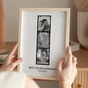 May include: A framed black and white print with three vertical photographs. The print is in a light wood frame. The text "BEST COUSIN MOMENTS" and "KEVIN & EMILY" are printed at the bottom of the print.