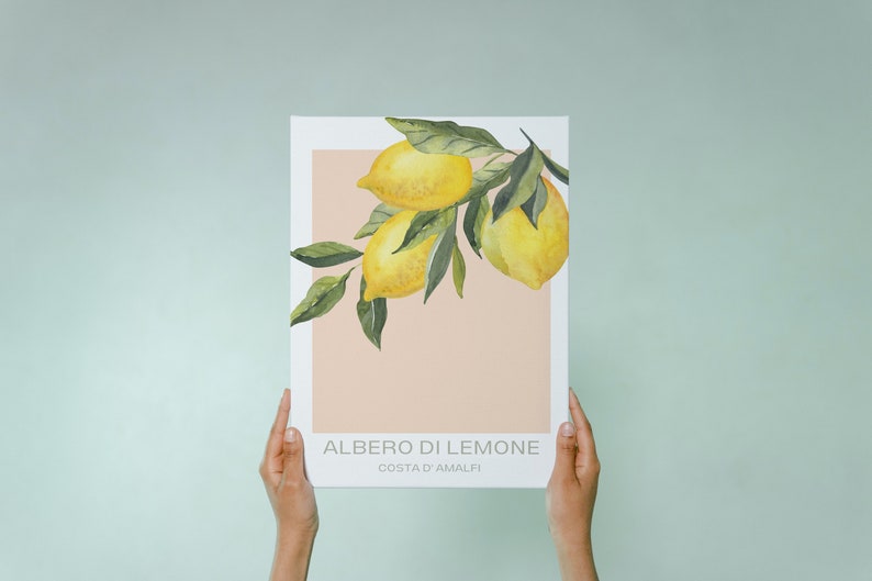 Op de afbeelding: Een aquarelprint van een tak van een citroenboom met gele citroenen en groene bladeren. De print heeft een perzikkleurige achtergrond en de tekst "ALBERO DI LIMONE COSTA D'AMALFI" onderaan.