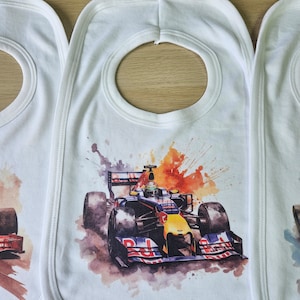 May include: Three white bibs with a colourful watercolour design of a racing car. The bibs have a round opening for the neck.
