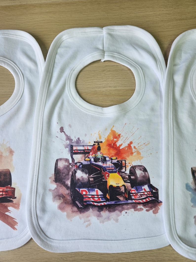 May include: Three white bibs with a colourful watercolour design of a racing car. The bibs have a round opening for the neck.