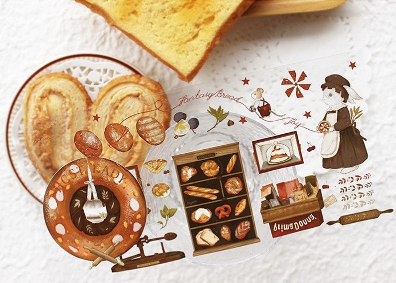 Op de afbeelding: Een set decoratieve stickers met een bakkersthema. De stickers bevatten afbeeldingen van brood, gebak, een bakkerijgevel, een windmolen, een muis en een vrouw in bakkerskleding. De stickers zijn gedrukt op transparant plastic en hebben een glanzende afwerking.