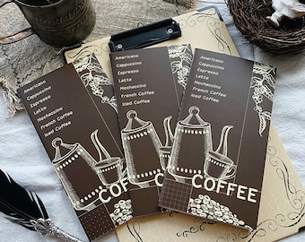 Puede incluir: Tres cuadernos marrones con temática de café. Cada cuaderno tiene una ilustración diferente de una cafetera y una taza. Los cuadernos tienen una lista de bebidas de café en la parte delantera: Americano, Cappuccino, Espresso, Latte, Mochaccino, Café francés, Café helado. El texto "COFFEE" está impreso en la parte inferior del cuaderno.