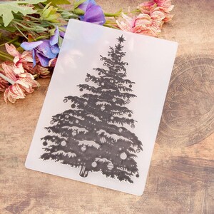 May include: A clear, rectangular embossing folder featuring a detailed Christmas tree design. The tree is decorated with ornaments and topped with a star. The design is in a dark gray color, perfect for crafting holiday cards and decorations.