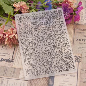 May include: A clear plastic sheet with a repeating pattern of black leaves and branches. The sheet is designed for crafting and can be used for scrapbooking, card making, and other paper crafts.