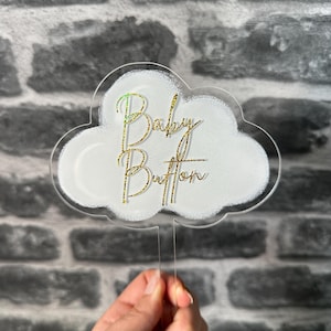 May include: A white acrylic cloud cake topper with gold glitter lettering that reads "Baby Button".