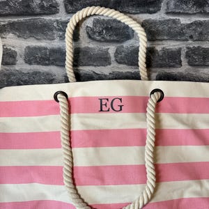 May include: A pink and white striped canvas tote bag with rope handles. The bag has the initials "EG" embroidered on the front.