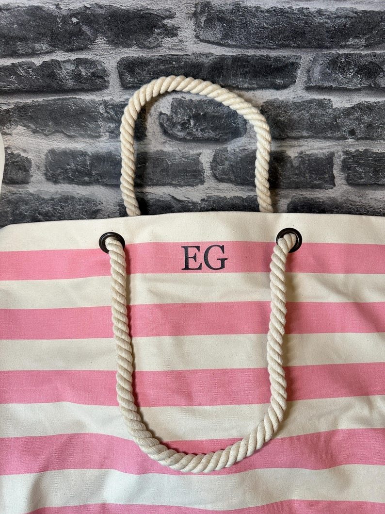 May include: A pink and white striped canvas tote bag with rope handles. The bag has the initials "EG" embroidered on the front.