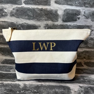 A white and navy blue striped canvas zippered pouch with the letters 'LWP' in gold lettering.