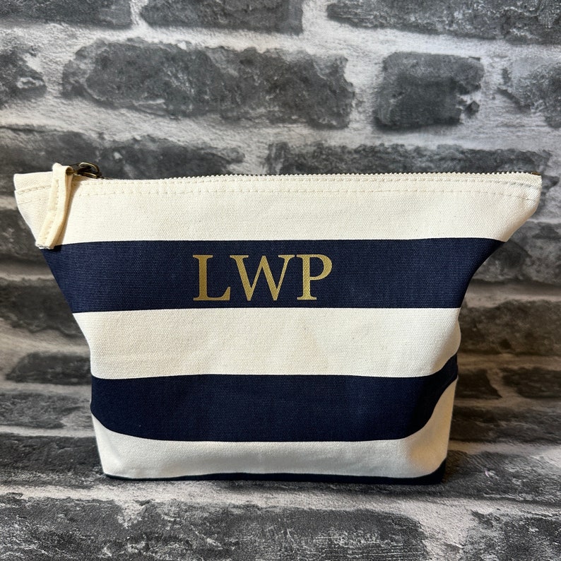 A white and navy blue striped canvas zippered pouch with the letters 'LWP' in gold lettering.