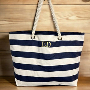 A blue and white striped canvas tote bag with rope handles. The bag has a gold monogram 'ED' on the front.