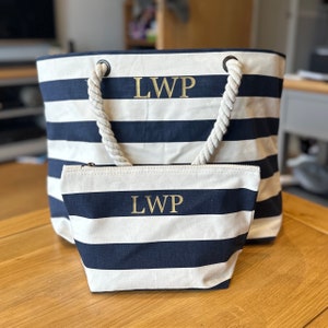 A striped navy blue and white canvas tote bag with rope handles and a matching zippered pouch. Both items are personalized with the initials 'LWP' in gold lettering.