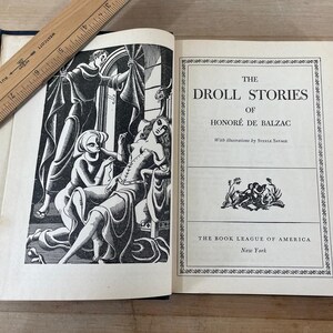 May include: An open book titled "The Droll Stories of Honor&eacute; de Balzac" with illustrations. The book has a black and white illustration on the left page and text on the right. A wooden ruler rests on the book.