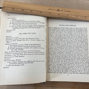 May include: An open book with text, a wooden ruler, and a dark blue cover. The ruler, marked in inches, rests across the pages. The text includes titles like "The Third Ten Tales" and "Translator's Preface."