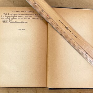 May include: An open book with aged, yellowed pages, titled "CAPTAINS COURAGEOUS." A wooden ruler, marked in inches, rests diagonally across the pages. The text "THE END" is visible.