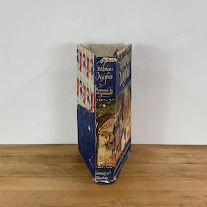 Könnte beinhalten: Ein Vintage-Hardcover-Buch mit dem Titel "Arabian Nights" mit Illustrationen. Das Buch hat einen blauen Einband mit goldener Schrift und dekorativen Mustern. Der Buchrücken zeigt Titel und Autor, mit Gebrauchsspuren.