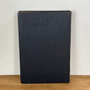 May include: A vintage book with a textured, dark blue cover. The spine shows signs of wear, with a slightly faded appearance. The book is standing upright on a wooden surface, suggesting it's part of a collection or display.