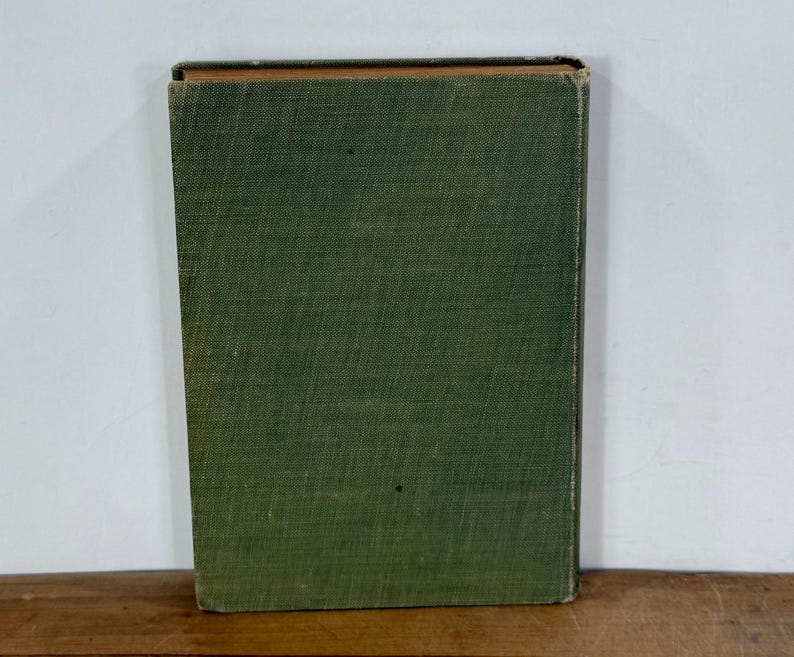 K&ouml;nnte beinhalten: Ein rechteckiges Hardcover-Buch mit einem strukturierten, olivgr&uuml;nen Stoffeinband. Das Buch ist vertikal aufgestellt und zeigt den Vorderdeckel mit sichtbaren Abnutzungserscheinungen an den Kanten und Ecken sowie einen dunklen Buchr&uuml;cken.