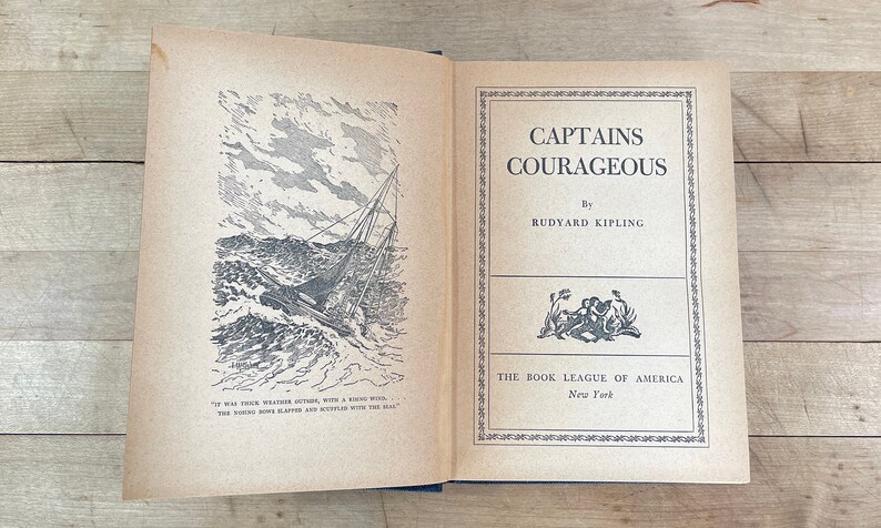 May include: Open book titled "Captains Courageous" by Rudyard Kipling. The cover features a black and white illustration of a ship at sea. Published by The Book League of America, New York.