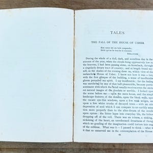 K&ouml;nnte beinhalten: Ein aufgeschlagenes altes Buch mit cremefarbenen Seiten und dunkelgr&uuml;nem Einband. Die rechte Seite zeigt den Titel TALES, den Untertitel THE FALL OF THE HOUSE OF USHER und einen gedruckten englischen Textabschnitt, der mit During the whole of a dull beginnt.