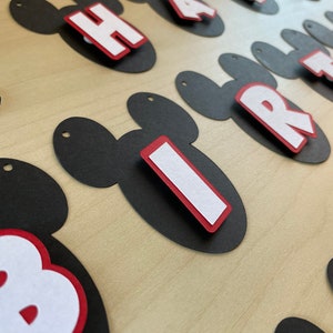 May include: Black and red Mickey Mouse-shaped paper cutouts with white letters spelling out "Happy Birthday".