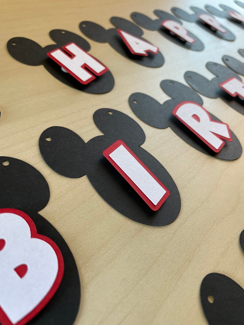 May include: Black and red Mickey Mouse-shaped paper cutouts with white letters spelling out "Happy Birthday".